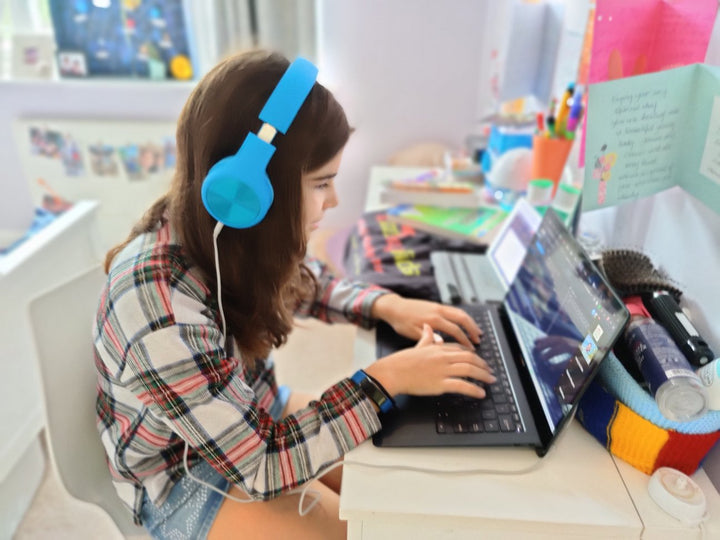 A learner with blue headphones coding on a laptop at home